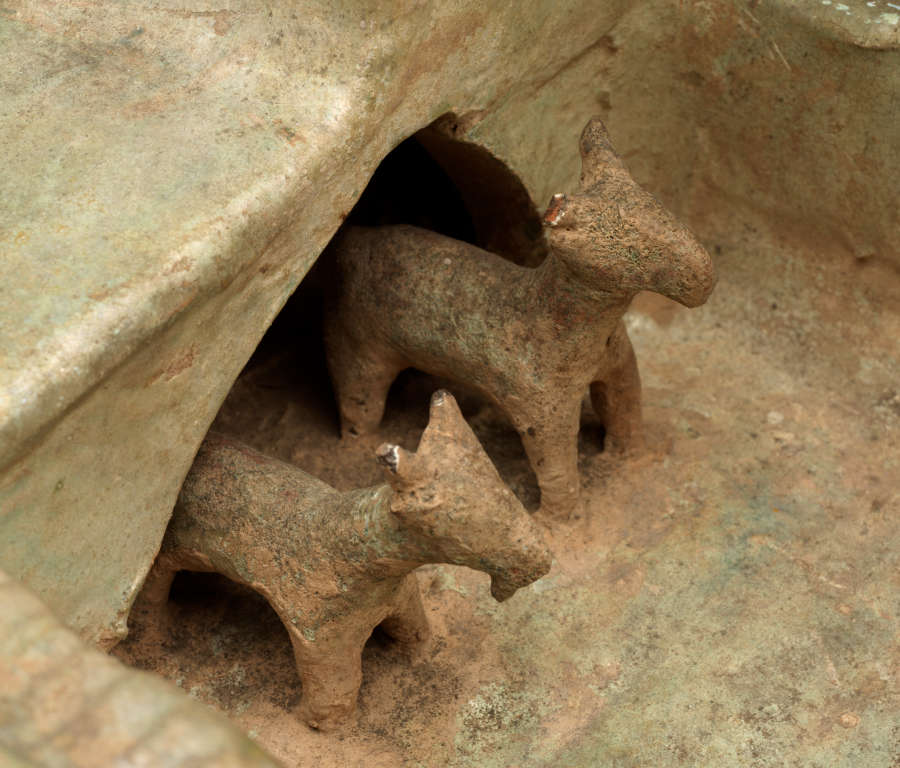 Detail of the ceramic sculpture of a walled farmyard, showing two small cattle-like animals standing in an arched doorway opening into the courtyard from a room.