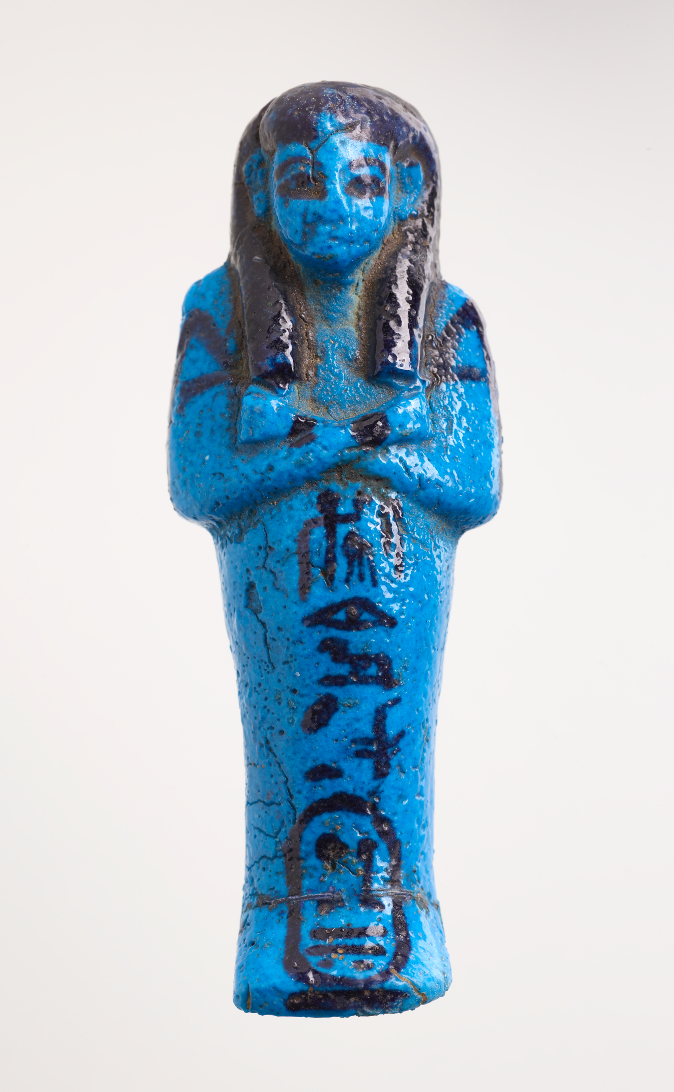 Front of a blue sculpture of a mummy-like figure with hands laid on its chest, with black detailing and hieroglyphic writing trailing down the length of its body laid horizontally.