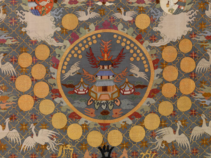 Centre of the robe’s back, featuring illustrations of pagodas with fiery wings encircled by a golden border and concentric rings of golden circles surrounded by white birds and earthy-pastel clouds.