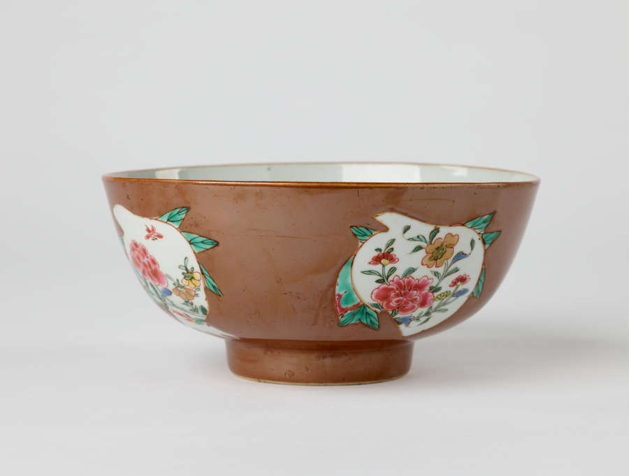 A white and brown bowl with green, yellow, and pink floral decorations with a short, small foot.