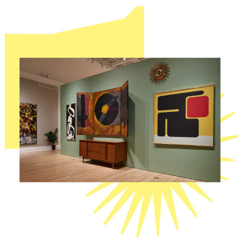 Modern paintings and furniture are displayed in a gallery space with pale green walls and wooden floors.