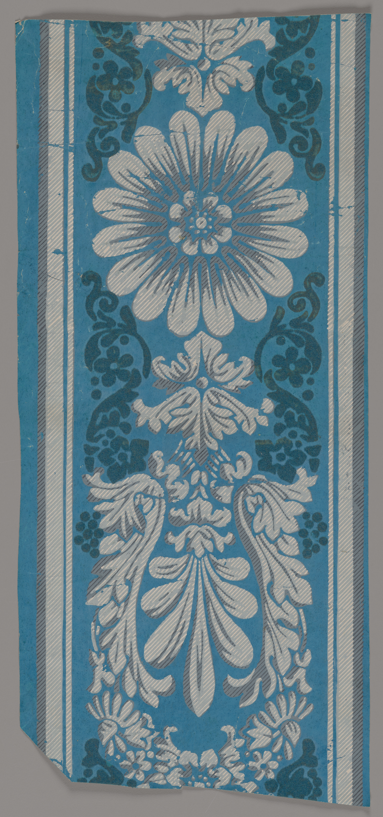 Central white flower surrounded by white and gray floral ornamentation and bordered by white stripes set against a blue background.