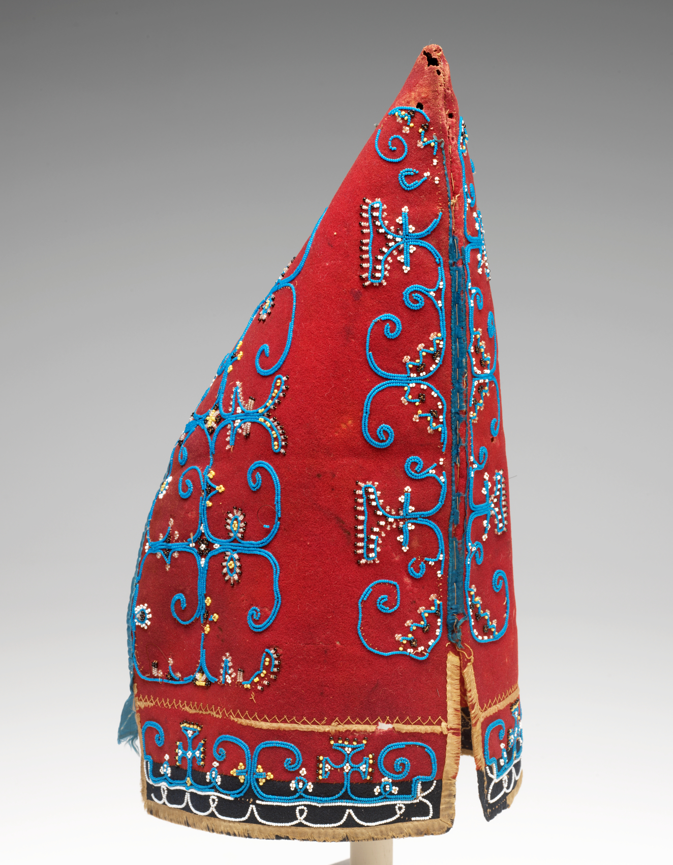 A pointed conical red hat with swirling blue embroidery with small pearl-like beads, and a slightly worn light yellow trim around the bottom edge.