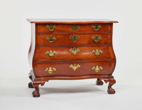 A polished wooden dresser with four curved drawers, ornate metal hardware, and intricately carved claw feet.