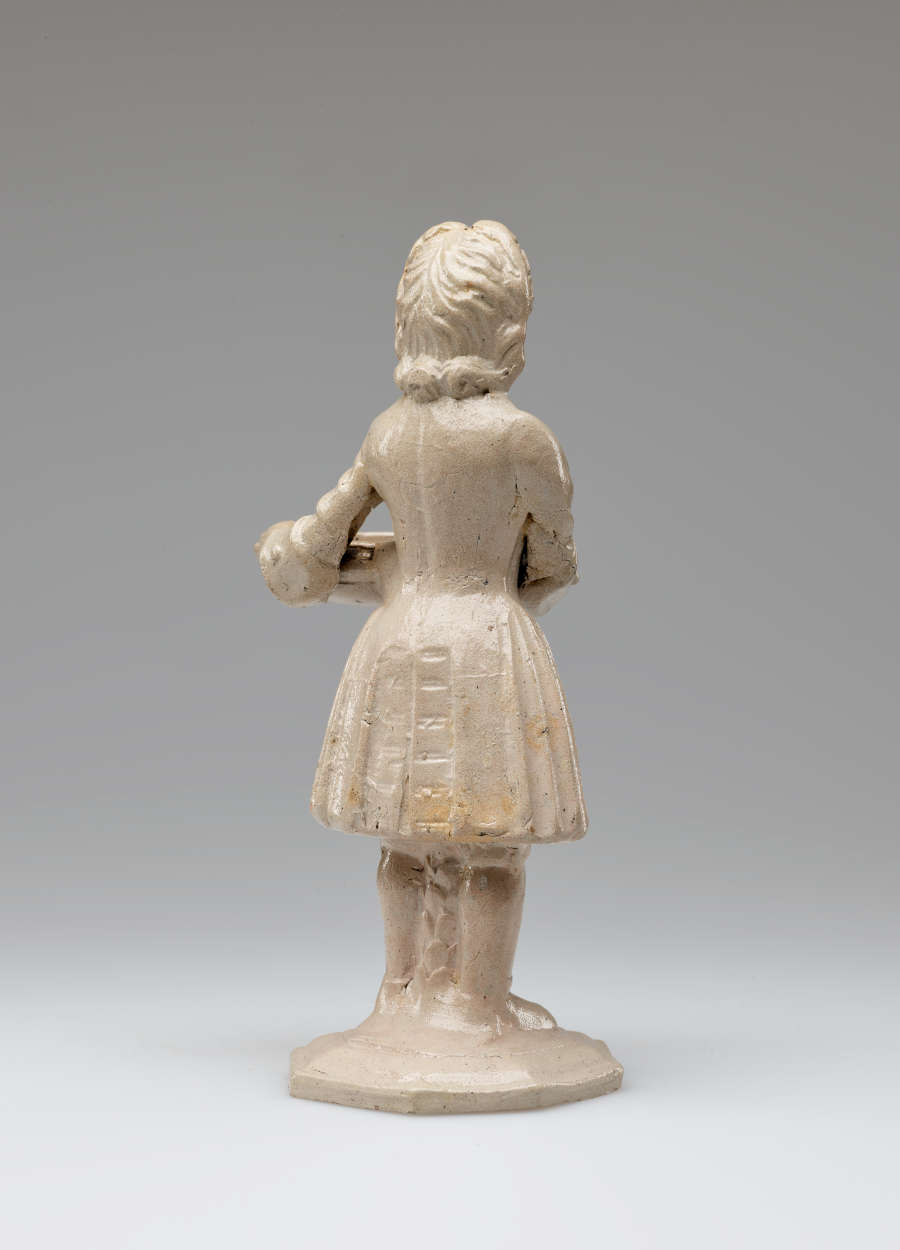 A cream colored sculptural figure holding a vessel, dressed in historical clothing with tightly curled hair.
