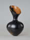 An asymmetrical, hourglass-shaped black vessel with a reflective finish. Its wide opening slopes down to the right, exposing a bright terracotta interior.