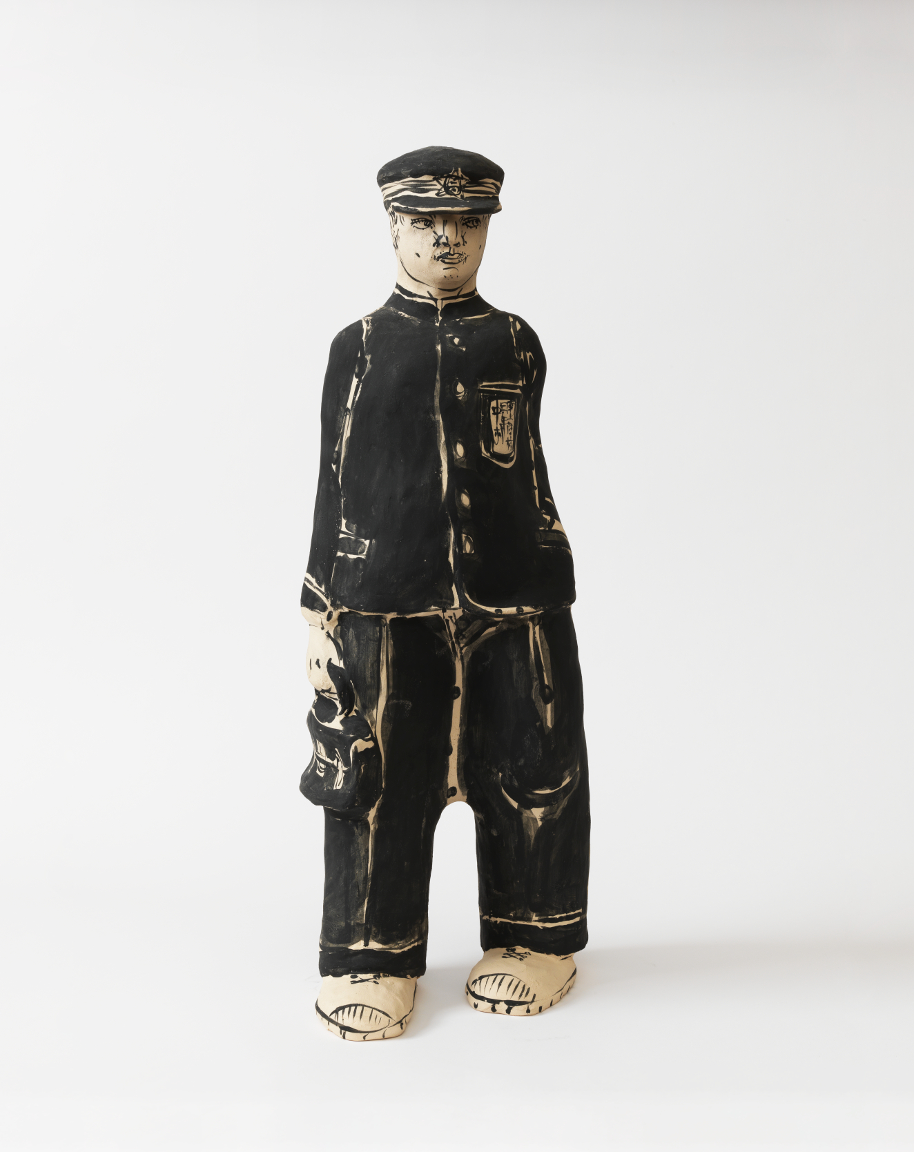 Stylized ceramic figure of a young man in a black uniform and cap, his features outlined with bold strokes, standing upright and carrying a small satchel at his side.