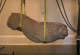 Stone lion sculpture suspended by straps in a softly lit room.