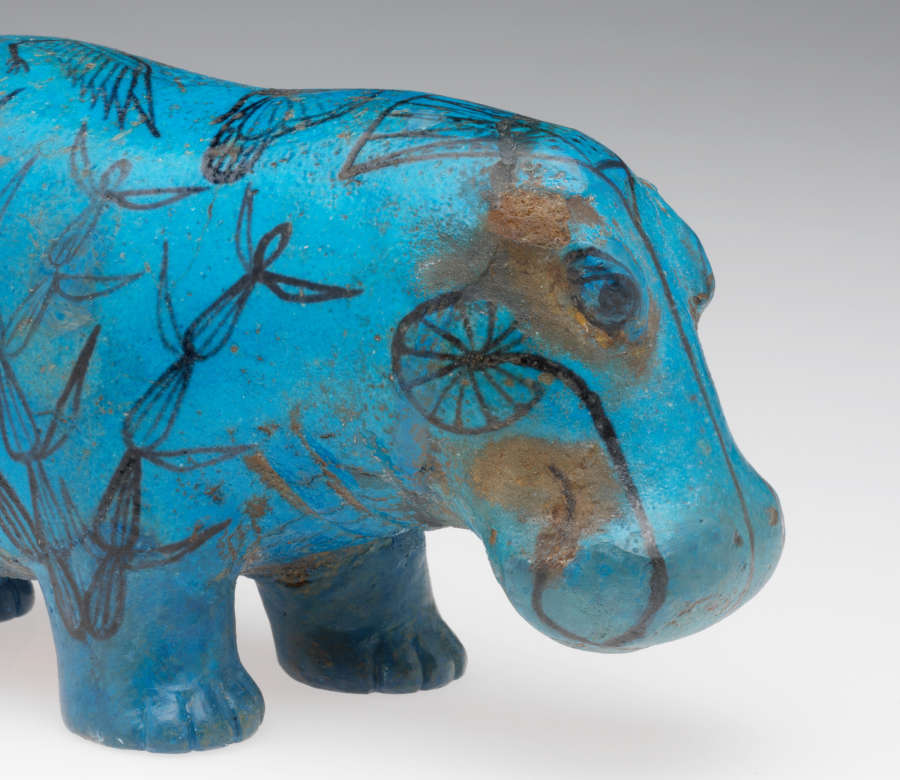 Front half of a hippopotamus figure covered in turquoise-colored glaze. It is decorated in delicate black line drawings of butterflies and lotus and papyrus plants from its Nile River habitat.