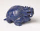 A quarter view of a blue sculpture of a horned tortoise, whose surface is covered with carved geometric patterns.