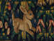 Detail of a tapestry featuring a golden rabbit mid-leap surrounded by vibrant, yellow, green, and red florals set against a dark background. 