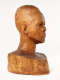 Three quarter front view of a glossy wooden bust depicting the head of a male figure with afrocentric facial features. He has a stern expression and an intense gaze.