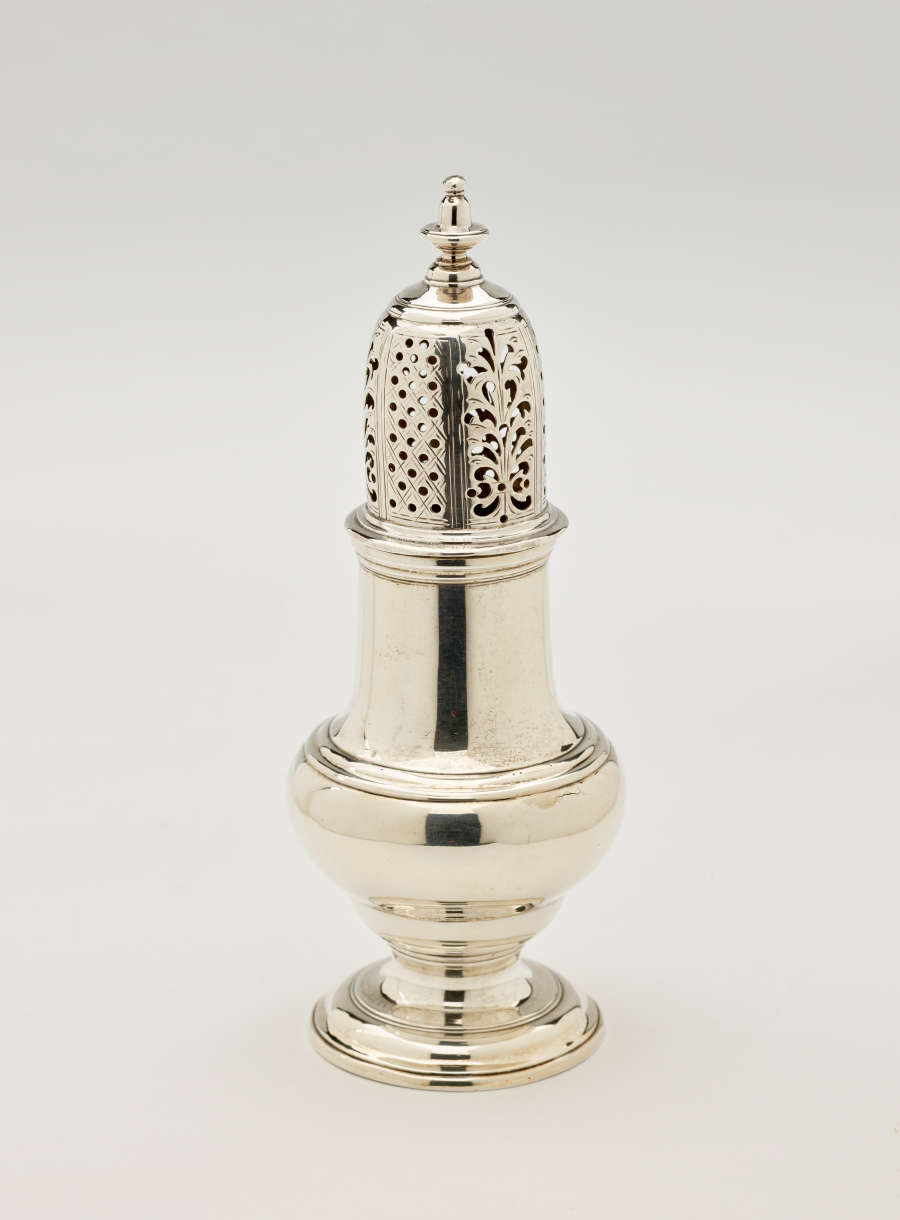 A silver vessel with a foot, rounded body that goes to a cylindrical top half, and the lid is perforated with small holes and floral cutouts.