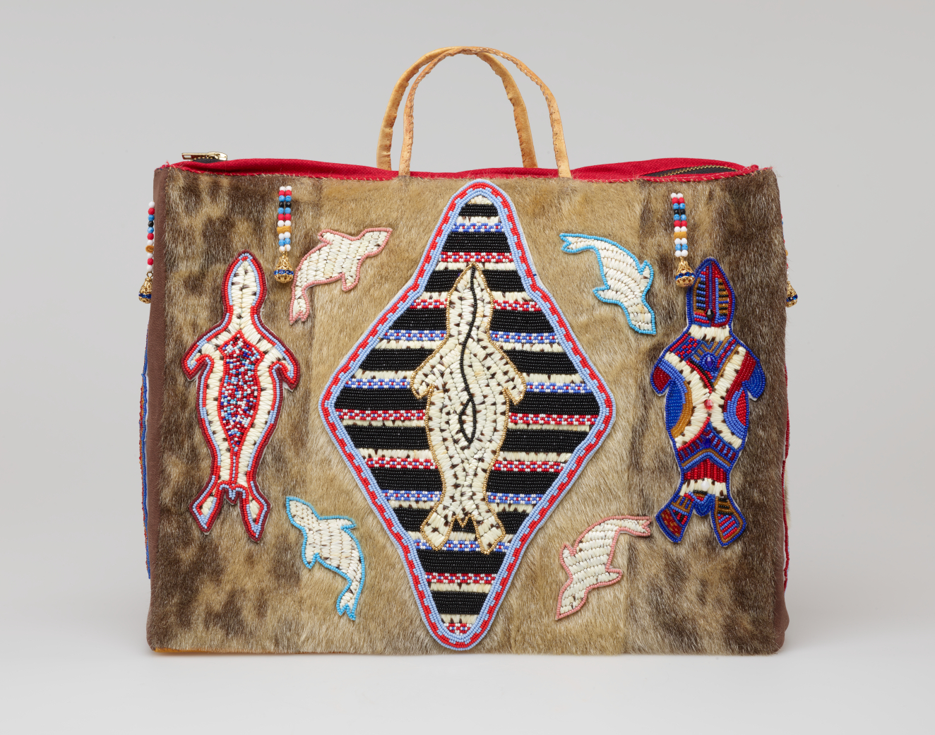 Fur-covered rectangular bag with thin looped handles, featuring central beaded seal silhouette within a black striped diamond, surrounded by red-blue patterned seals and multi-colored tassels, including a brown side panel. 