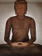A weathered wooden Buddha statue sat in meditation, with his hands resting in meditation and a soft, serene expression.