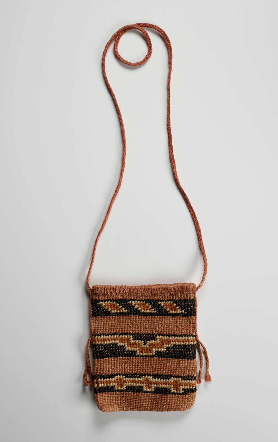 Woven rectangular bag with a long strap laying flat on the white backdrop. Its body features three rows of terracotta separated by three rows of yellow bordered terracotta geometric patterns against black.