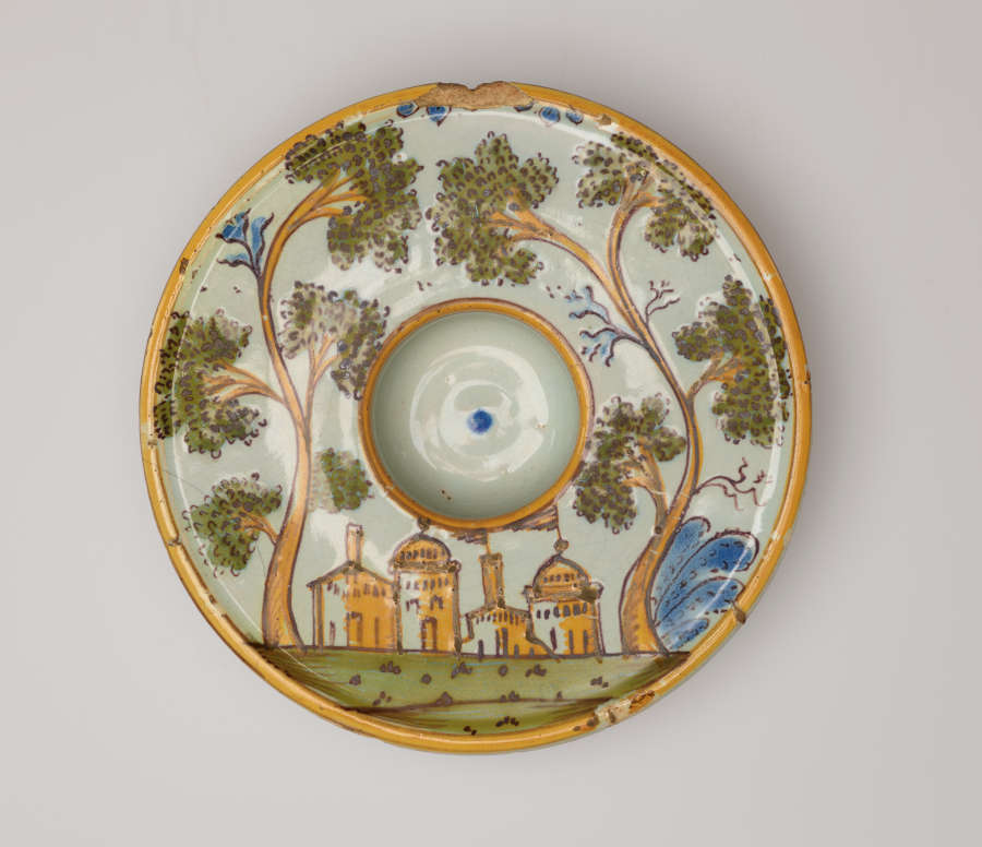 Round plate decorated with an image of buildings and trees. There is a concave well in the center of the form.