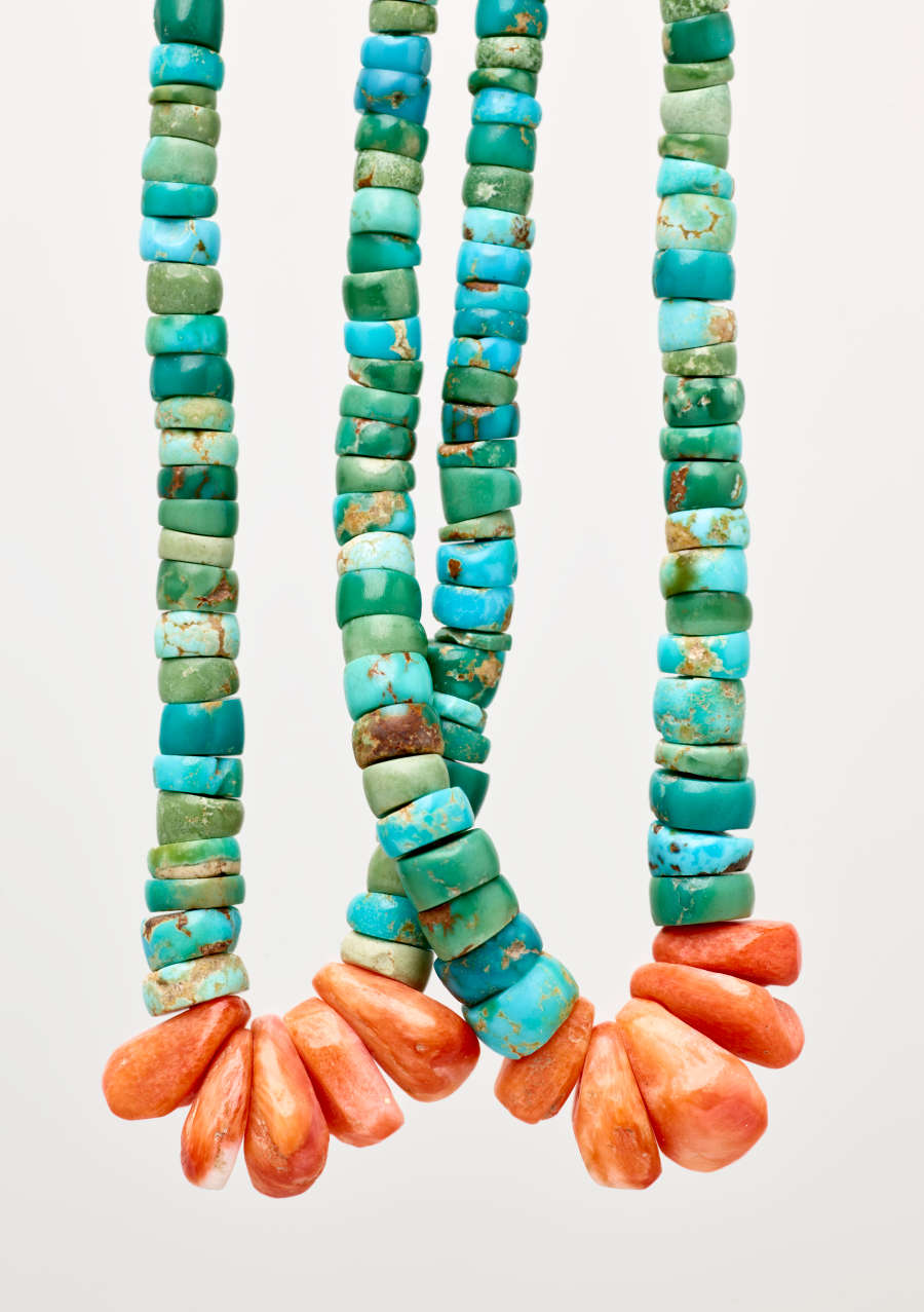 Close-up of the earring’s two loops of flat, circular, uneven turquoise beads, with kernel-like red beads at each loop’s base. Visible are golden flakes on the turquoise beads.