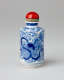 A bottle with delicate swirling blue decorations and a rounded, shiny red stopper.