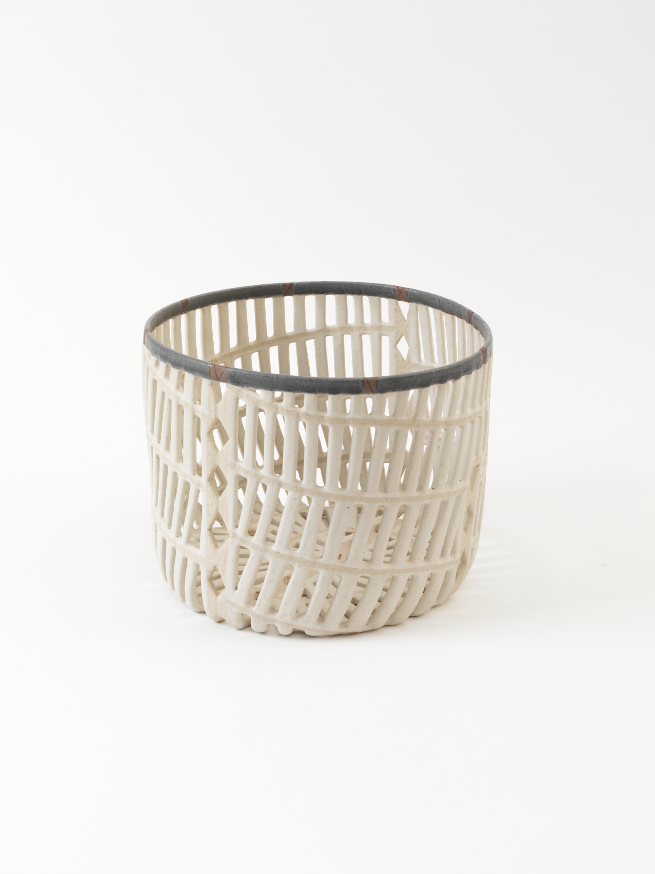 Delicate white basket-like cup constructed of intersecting lattices forming an airy woven grid with narrow open slats and a dark gray edge around the opening.