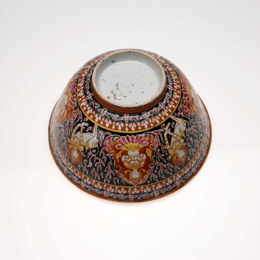 Bottom-view of a circular bowl. Its round base is white. Its body features a row of sitting figurines surrounded by red, against blue patterns, framed by red and blue motifs.