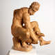 Realistically carved terracotta sculpture depicting a muscular bearded man sitting and leaning over to hold a vessel between his legs, one of which is wrapped over top of it.