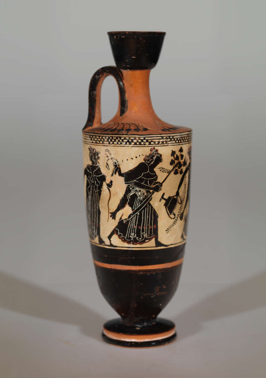 Tall vase with a slender neck. Its tan-orange surface is decorated with black illustrations of robed figures walking and carrying branch-like objects and jars, as well as stripe patterns.