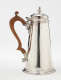 A silver chocolate pot with a spout, hinged lid, and fruitwood handle that is 90 degrees from the spout.
