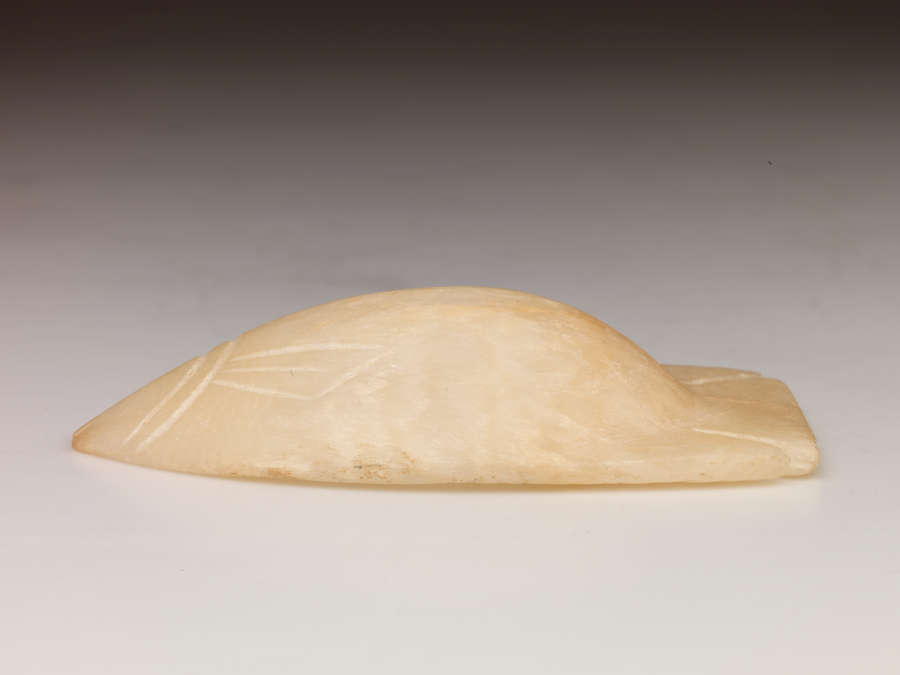 Side view of the tan bowl upside-down, showing that part of the bowl shaped as the tail of a fish extends further outwards than the rest of the bowl.