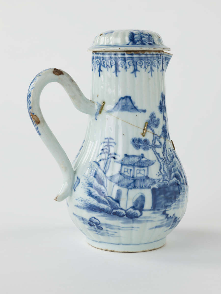 A white chocolate pot with blue decorations depicting floral and architectural elements.