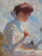 Profile of a seated woman in quiet focus, her head bowed and hands poised near her chest. She sits on a sandy hillside beneath a blue, cloud-filled sky.