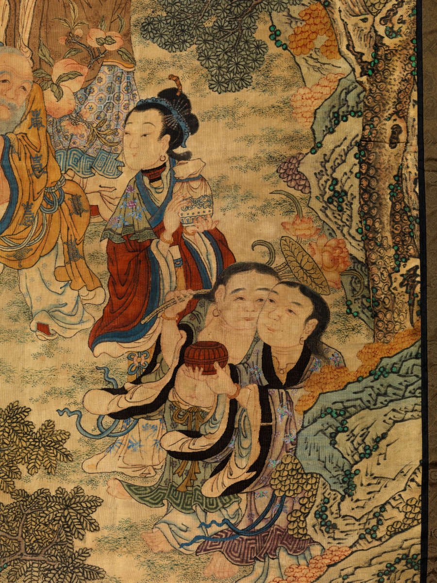 Detailed view of two sitting figures and one standing figure behind them. The standing figure looks leftwards while the two sitting figures engage with each other.