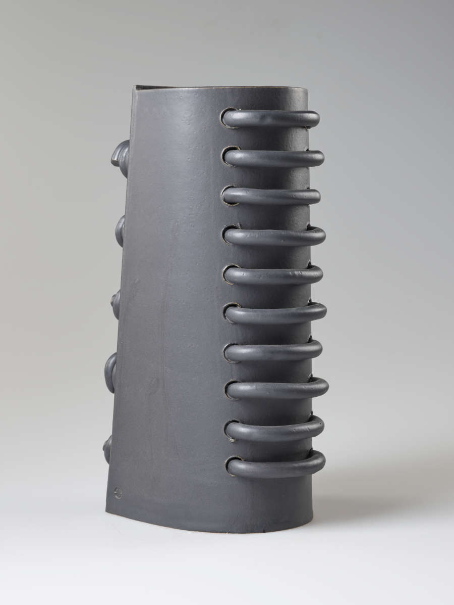  Back view of a gray industrial-like cylinder with one flat periphery. Ten large vertically aligned loops are threaded through and protruding from the rounded back side
