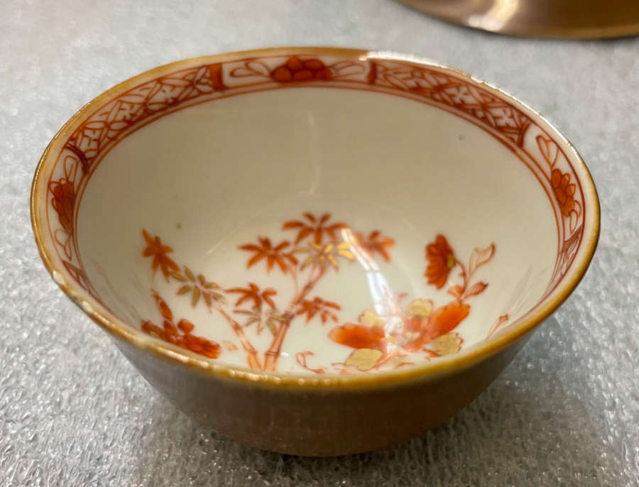 A small ceramic bowl with a golden exterior and intricate red floral designs on the white interior, bordered by a red geometric pattern.