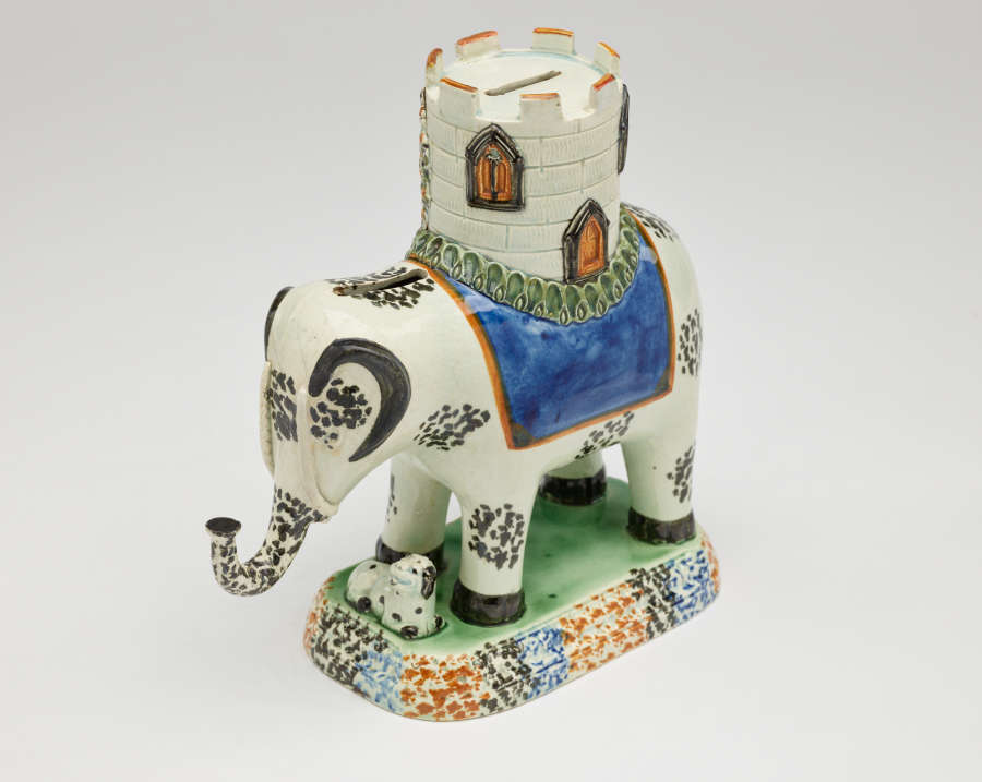  A sculpture in the shape of an elephant with a castle on its back. The decorations are white, blue, green, and yellow.
