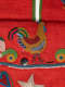 Detail of the red bag's body, showing an intricately beaded chicken as well as a small button and a cream lined embellishment sit in between the blue rimmed bag opening.