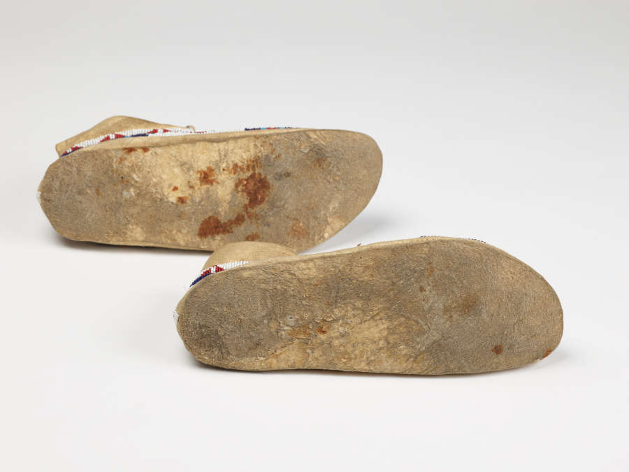 Dirty and worn gray and yellow soles of a pair of moccasins, highlighting the soles’ red markings.