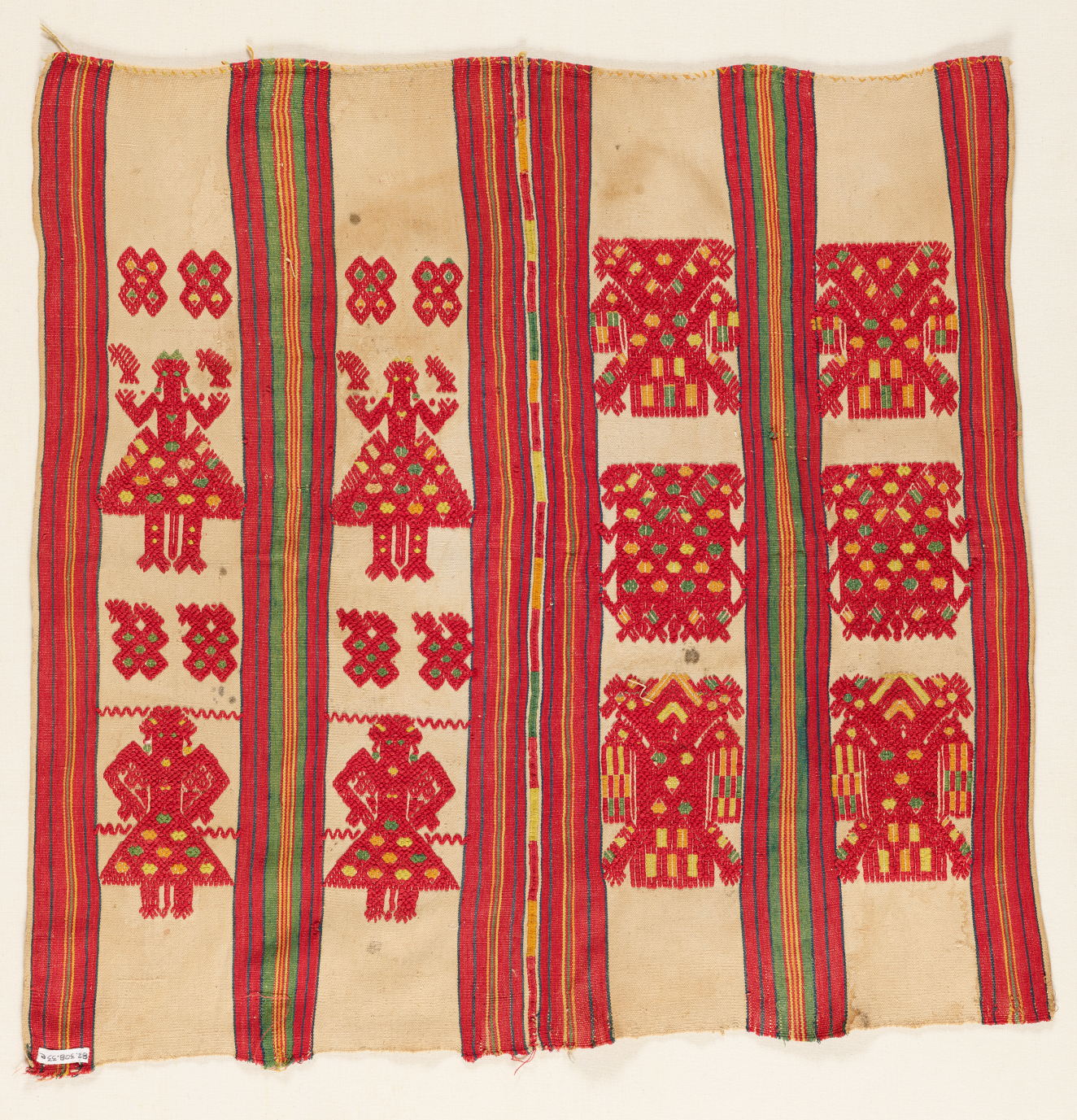 A woven textile of red figures and abstract shapes arranged in vertical bands separated by vertical red bands with multi-colored stripes on a beige cream colored. 