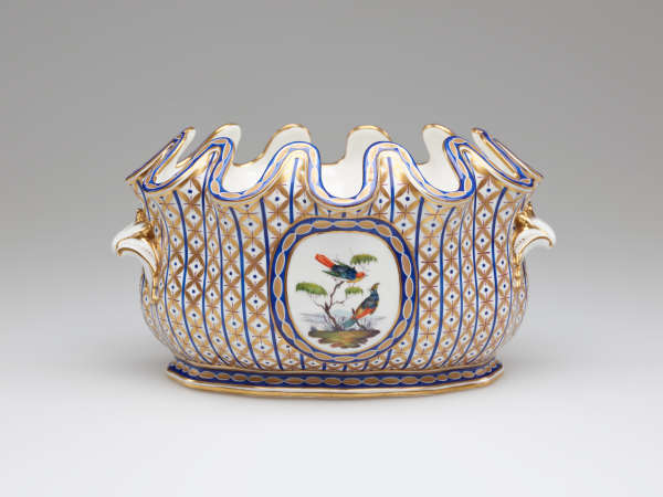 An open vessel with a deeply scalloped rim. A central decoration of two birds and a tree is surrounded by vertical bands of blue with gold diamond shapes.