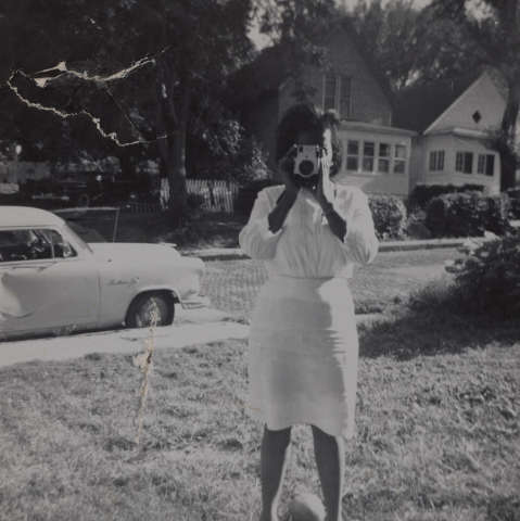 Black &amp; white snapshot of a young Black woman dressed in white taking a photograph