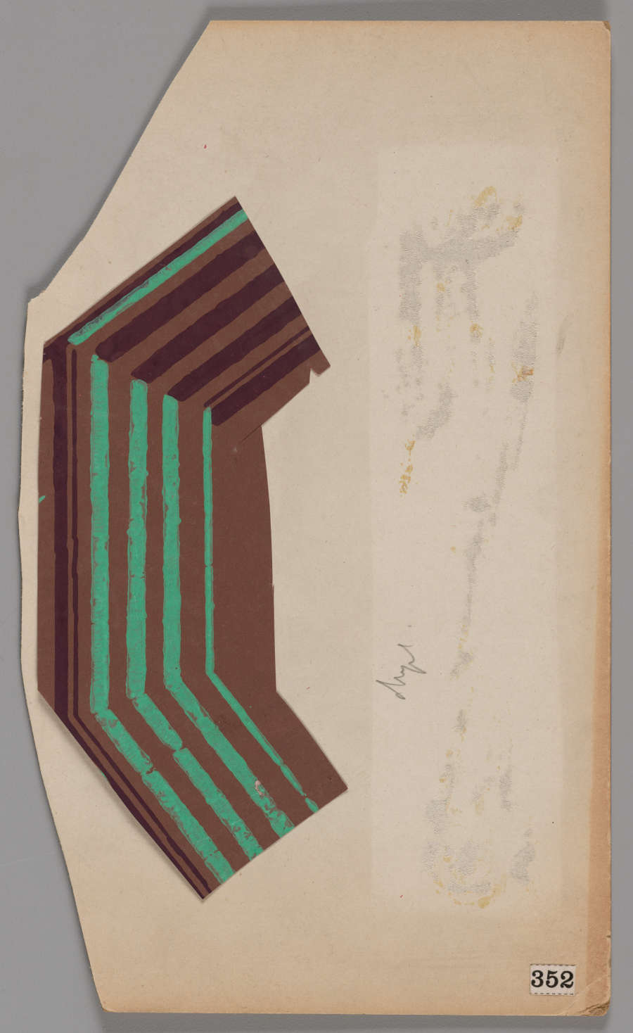 Paper cutout with a curved brown design featuring angular green and dark brown lines. To the right of the pattern is paper damage.