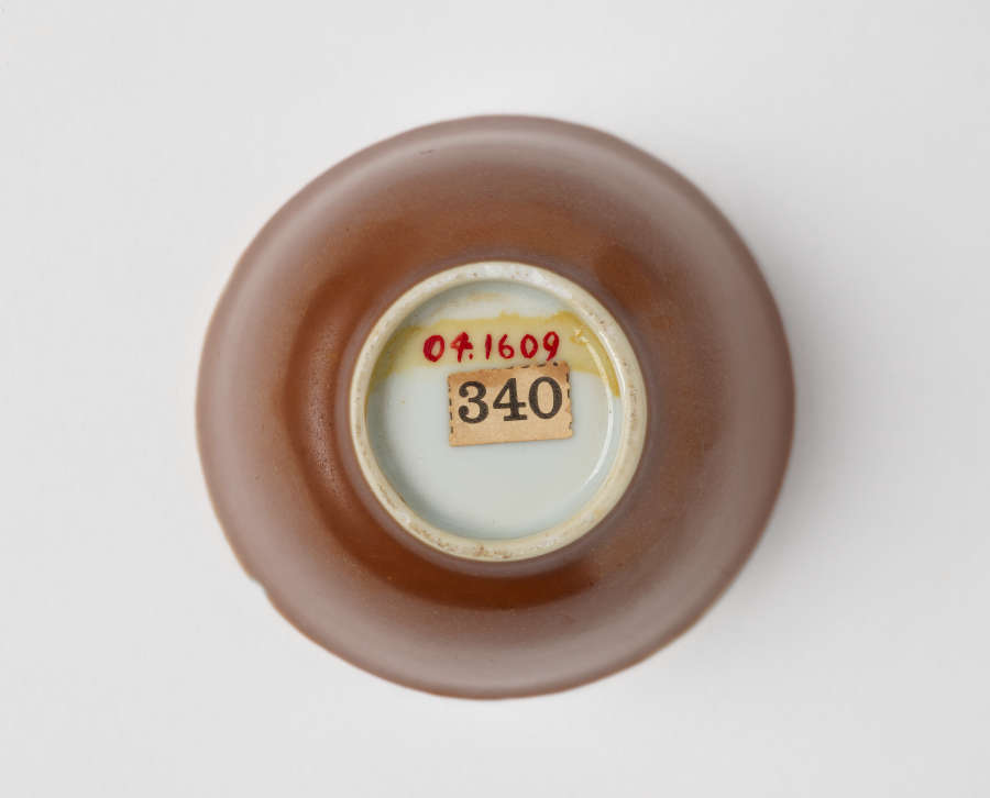 The underside of a small ceramic bowl with a gold exterior, with a white circular base marked with a label reading "340" in black and additional red markings.