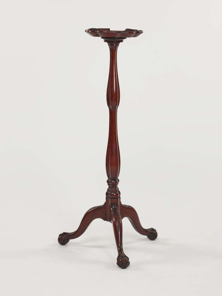 A tall, wooden candle stand with turned legs and ornate, tripod feet.