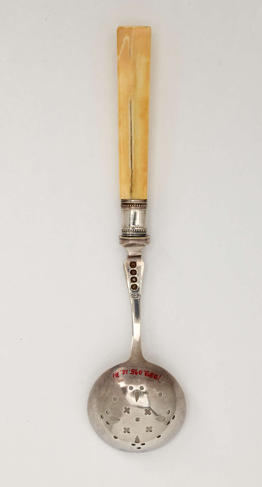 A metal tool with small cutouts in the bowl and an ivory handle.