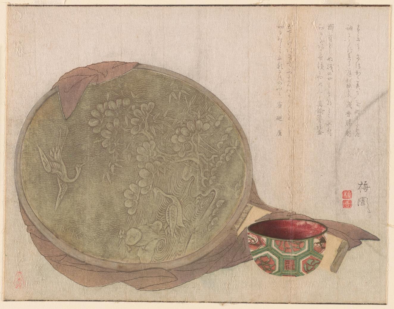An ornate bronze mirror with floral and bird engravings beside a red and green patterned bowl with columns of calligraphy. 