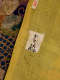 A close up of a yellow textile with visible seams and fibers and an affixed label with handwritten characters. 