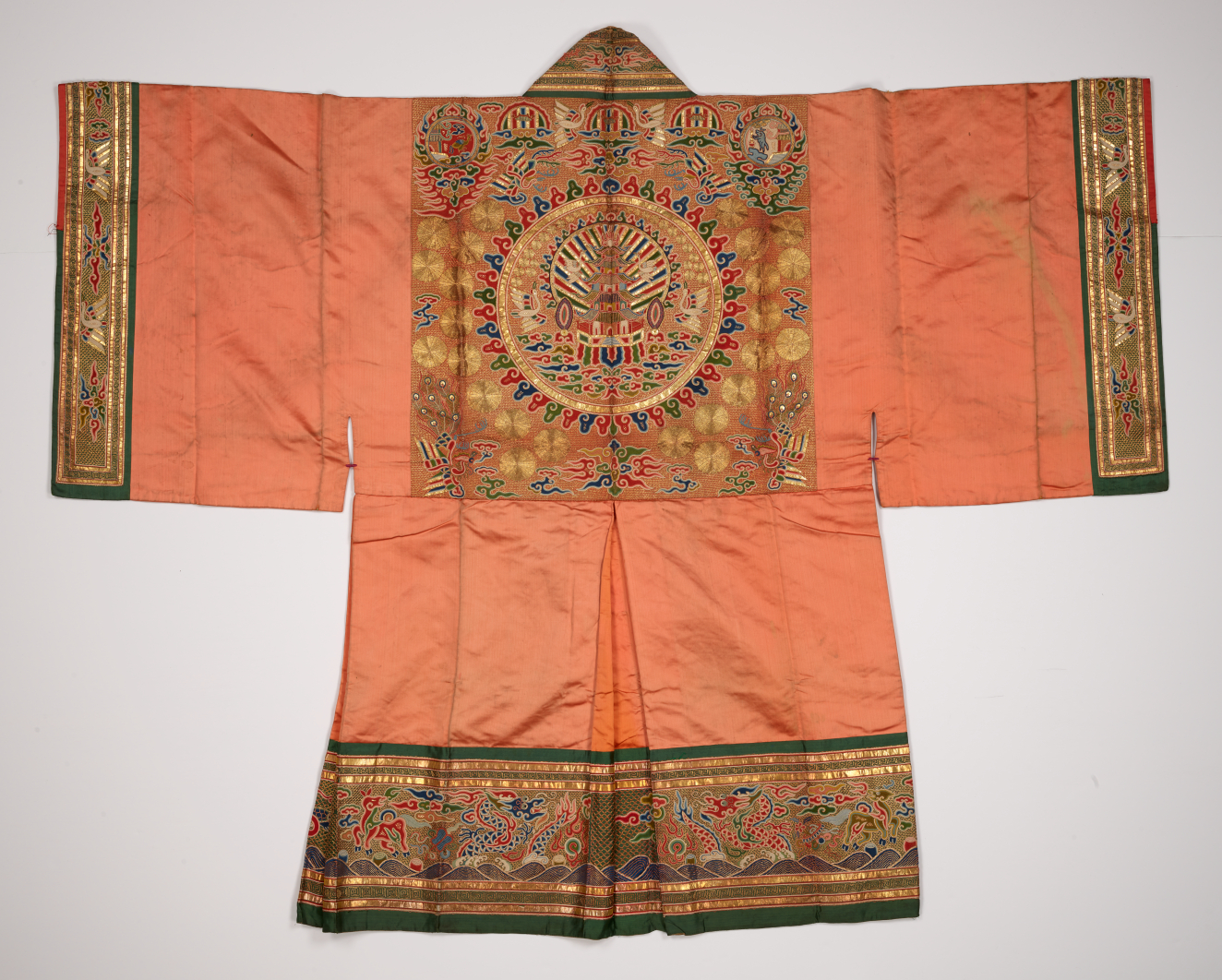 The backside of an orange robe laid flat with wide rectangular sleeves, gold-detailed embroidery along the sleeves, collar, and bottom hem, and a radiating circular design featuring a tiered building. 