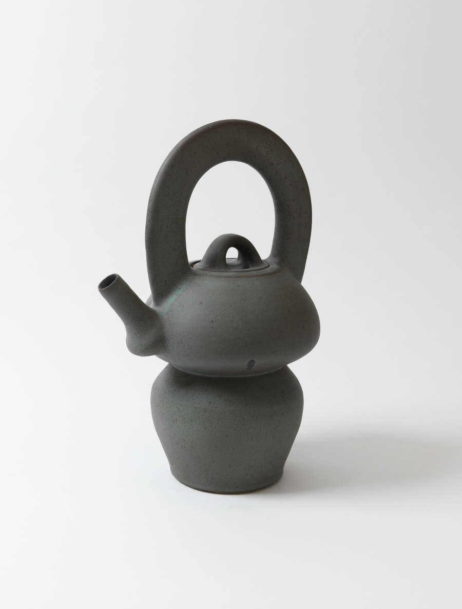A smooth, minimalistic dark gray teapot with a smooth matte surface, bulbous upper and lower sections joined by a narrow waist, and an oversized handle looping above the lid.