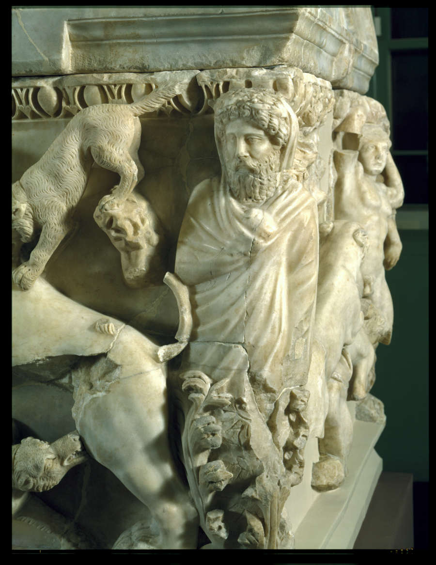 The edge of the stone coffin, featuring carvings of a bearded man in robes with pouncing animals on both sides.