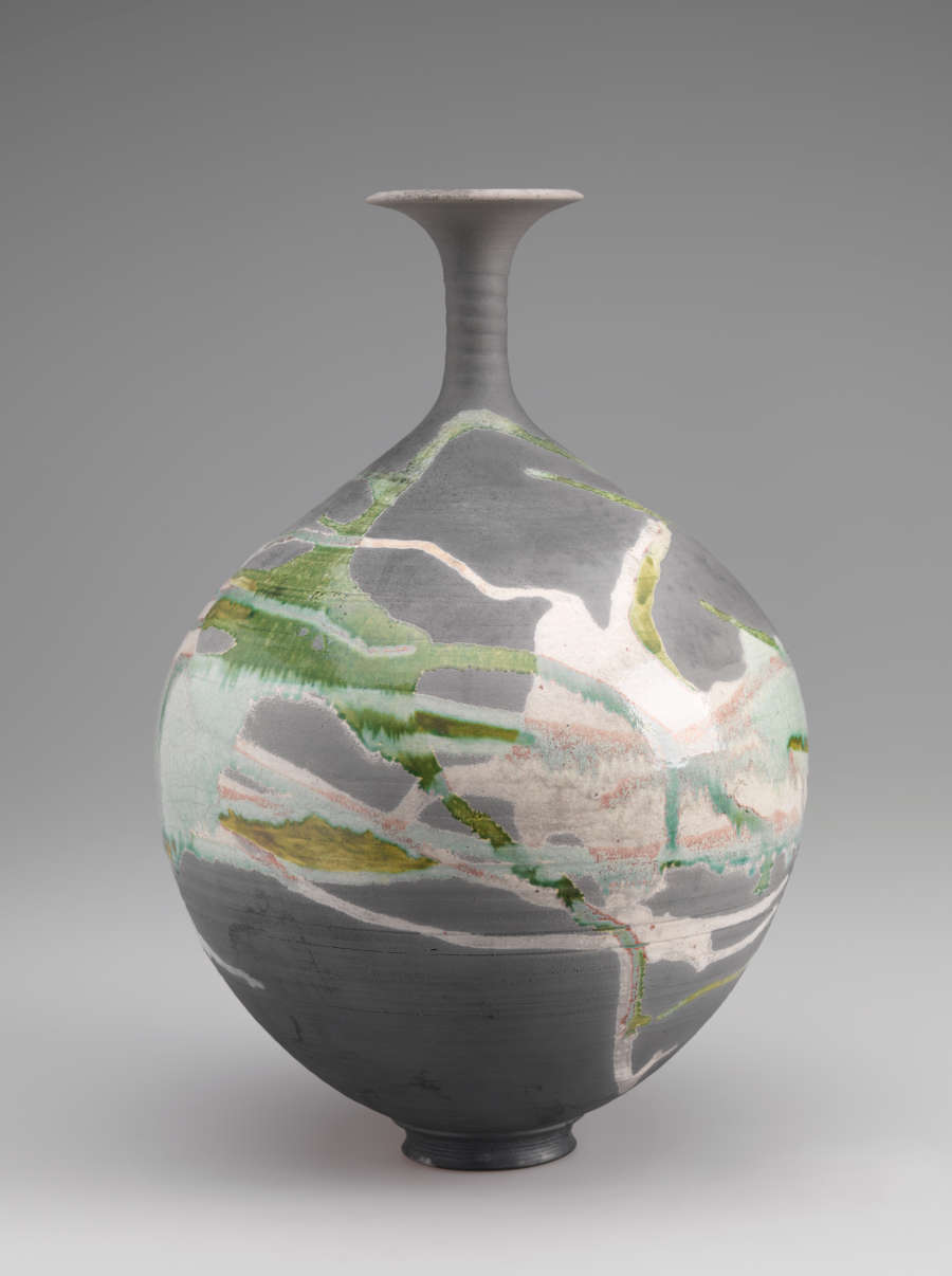 Bulbous gray vessel with skinny neck and flared top. Covered all the way around in splashes of green and pink glaze.